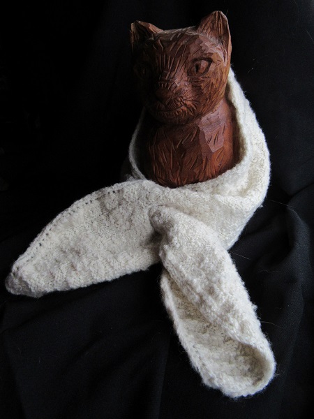 natural white scarf wrapped around a carved cat against a black background